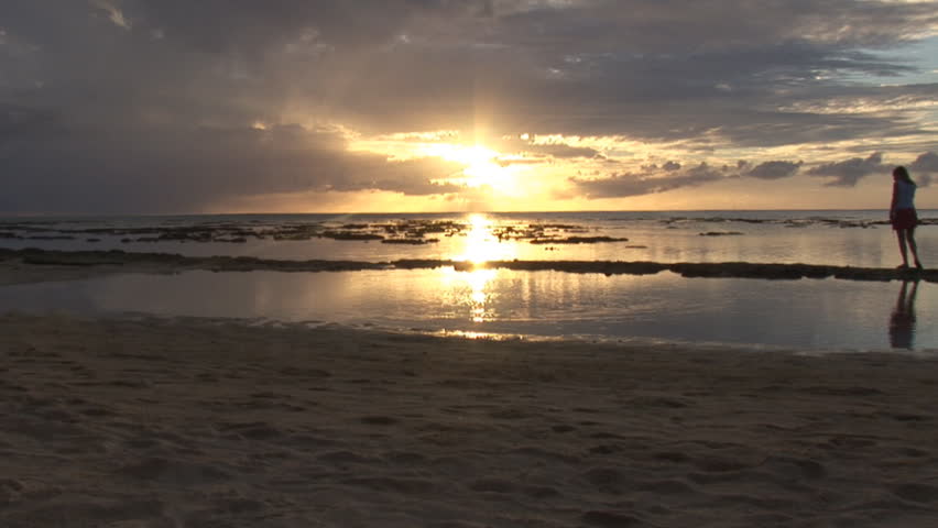 A woman walks alone along a tropical beach at Dusk