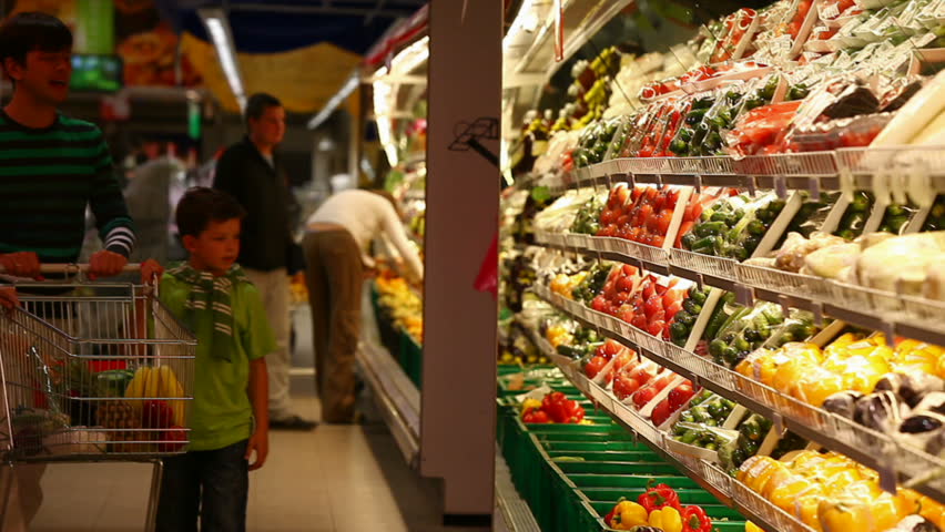 A family of four approaching vegetable row in the supermarket, taking some vegetables and placing them into the trolley