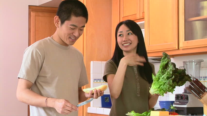 Happy young Asian couple preparing food in kitchen