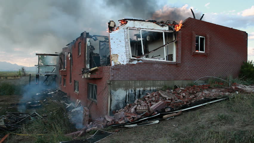 Fire burns a brick and wood house as firefighters stand back and let it finish burning. Brick collapsed as structure is weakened. Fire and smoke coming from many windows and openings.