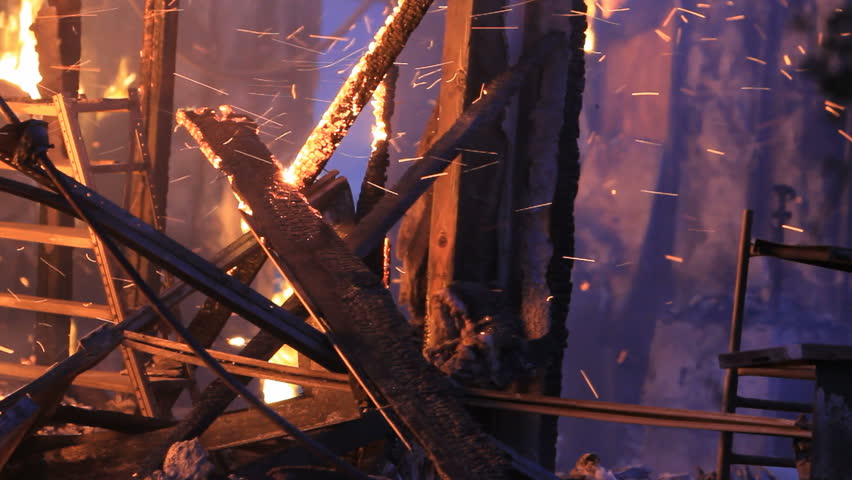 House totally destroyed by fire. Closeup of interior still burning with smoke, flames and sparks. After dark. 
