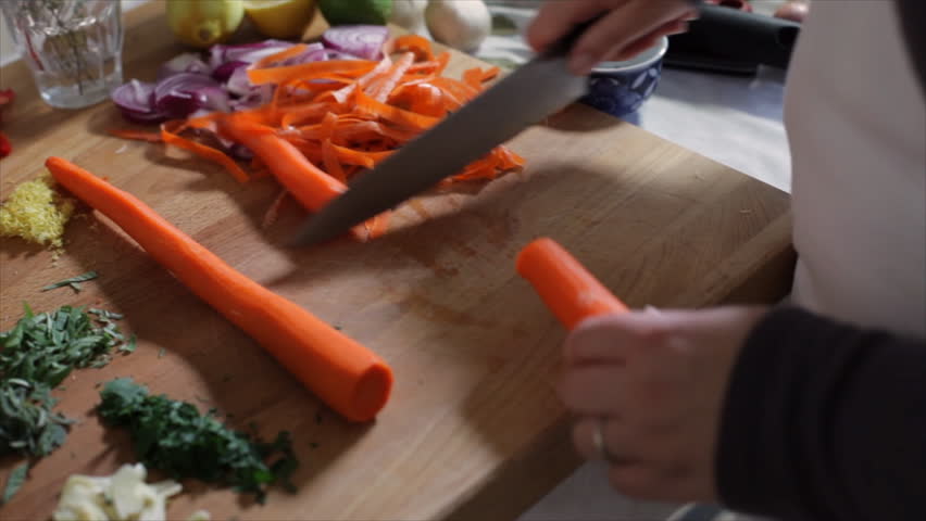 A chef slicing carrots that have already been peeled. Camera is hand held.