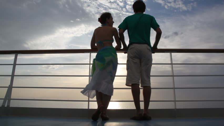 young couple stands on deck of cruise ship and talks against sunset sky