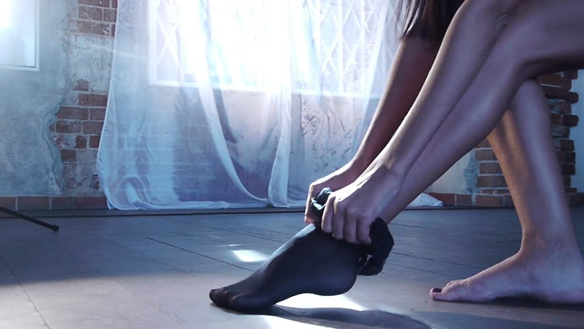 Girl sitting on chair and putting on black stockings.