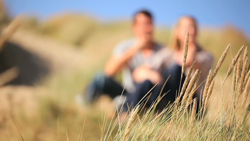 Attractive young caucasian couple enjoying quiet time together sitting in sand dunes at the coast