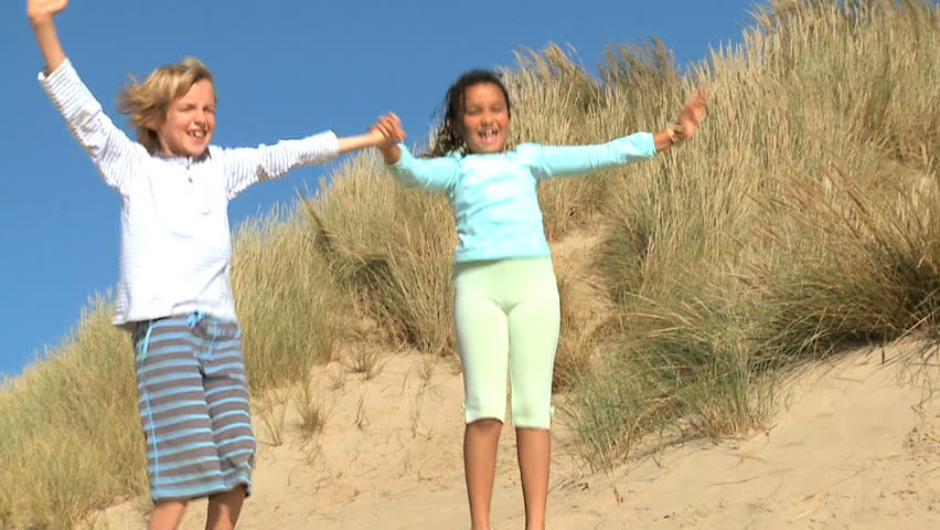 Mixed race childhood friends having fun playing in sand dunes by the coast filmed at 60FPS