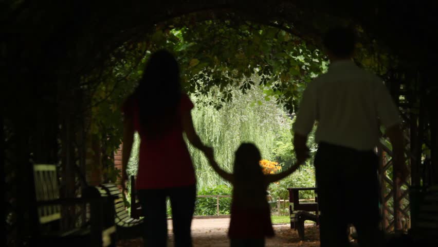 Family walks from one end of the tunnel to another in a park, silhouettes 