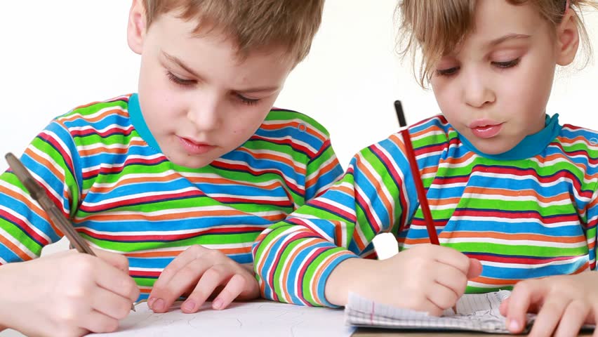 Little girl in a striped shirt with long sleeves and little boy with a chocolate-smeared mouth draw pictures in notebooks, sitting at desk