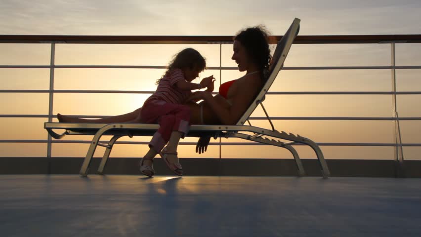 silhouettes of mother and daughter on deckchair of ship against sunset sky