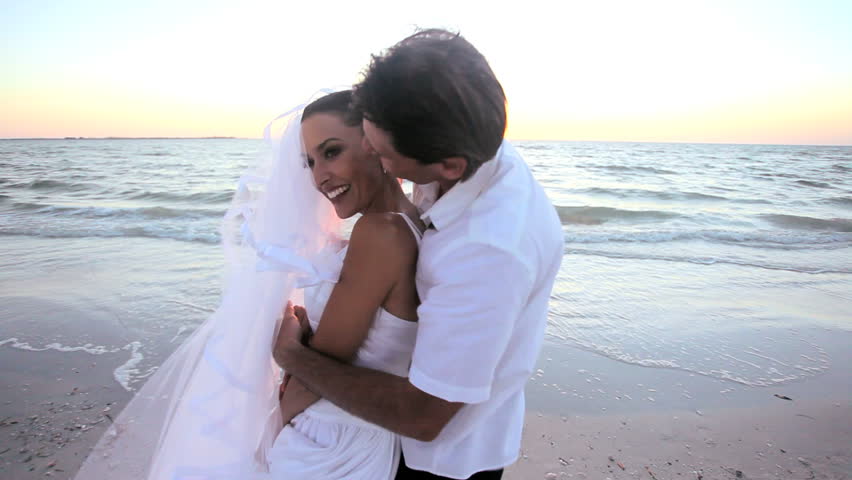 Attractive couple celebrate after their dream wedding on a beautiful sandy beach as the sun goes down
