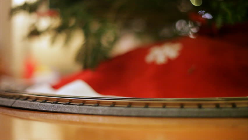 A bright colored toy electric train chugs along a track placed around the base of a decorated Christmas tree.