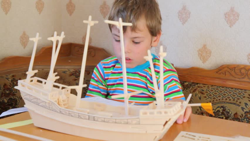 sitting boy attaching mast with flag to toy model of ship