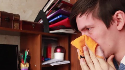 young guy has a runny nose, wipes his nose with a handkerchief, sneezes into his handkerchief