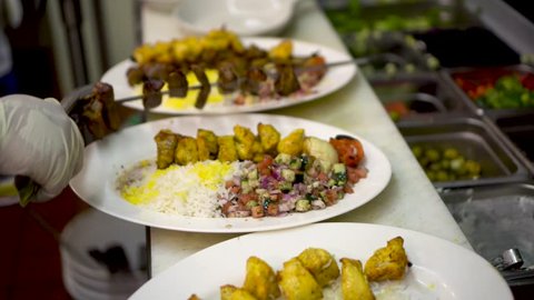 Chef slides beef kabob off of a skewer onto a plate with chicken kabob and rice with saffron.
