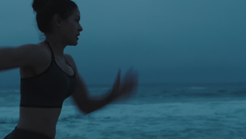 strong young woman running on stormy beach sprinting fast exercising cardio workout training focused female athlete runner in cloudy seaside background tracking close up