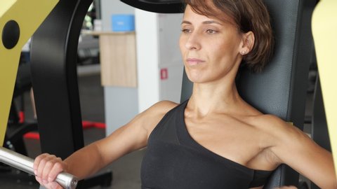 Portrait Of Slim Woman Is Doing Exercises For Arms Muscles On Training Machine She Is Sitting And Pushing Away Some Reps Sports Workout In The Gym