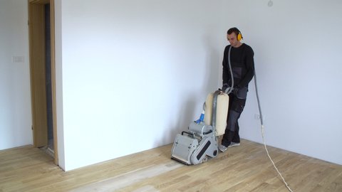 Scraping Hardwood Floor With The Grinding Machine Repair In The Apartment Carpenter Doing Parquet Wood Floor Polishing Maintenance Work By Grinding Machine