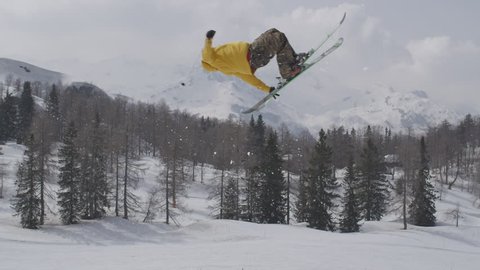 AERIAL SLOW MOTION: Freestyle skier jumping over big air kicker in sunny winter in ski resort