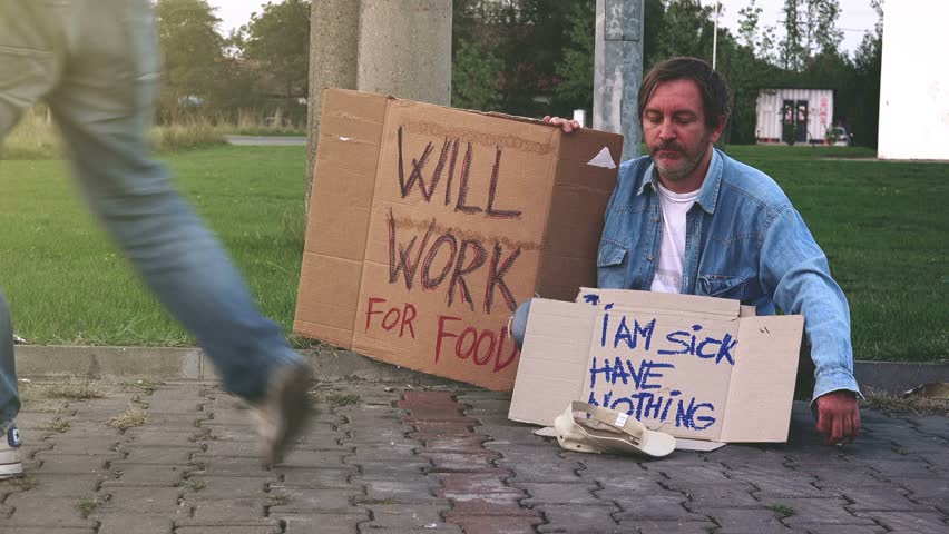 Homeless Man Stands At The Side Of The Road Holding A Sign That Says