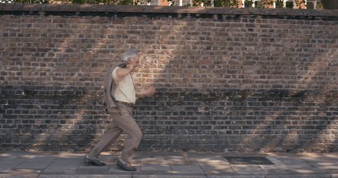 Contemporary happy elderly man wearing suit funky street dancer dancing freestyle in the city