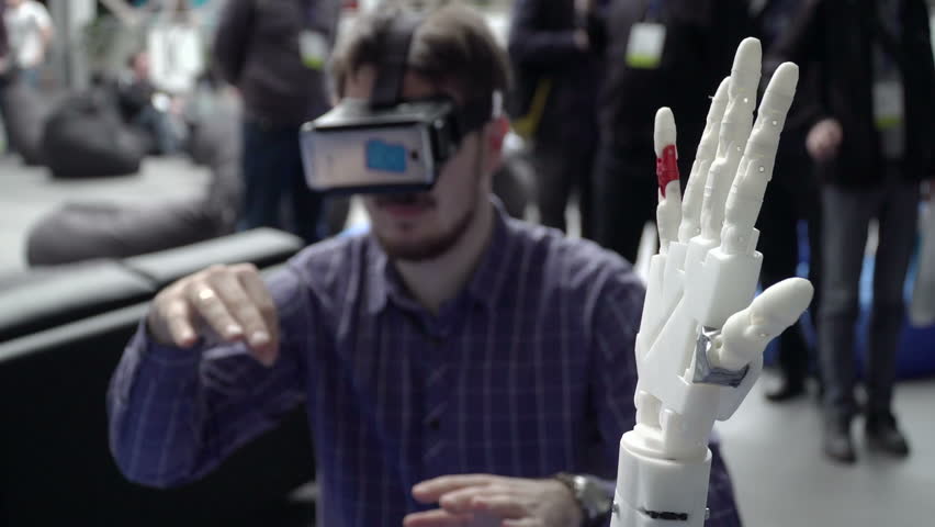 Cybernetic system today. Game industry and motion tracking in cyberspace. Man with innovative spectacles creates movement for mechanical plastic arm. Printing on the 3D printer. Sci Fi and prosthetics