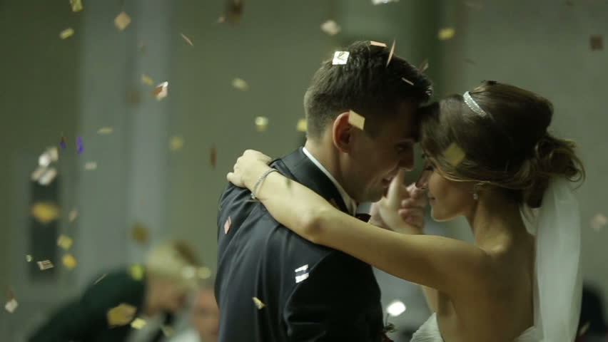 Beautiful brunette bride and handsome groom dancing first dance at the wedding party. Confetti in the air. Very tender moment