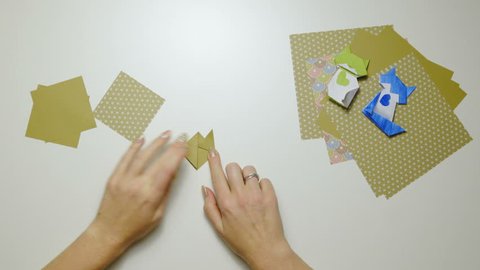 Origami Folding Cat Head On Table Top View 4k Big White Table With Origami Paper And Two Folded Cats Lying In Corner And Female Person Hands Folding A New Origami