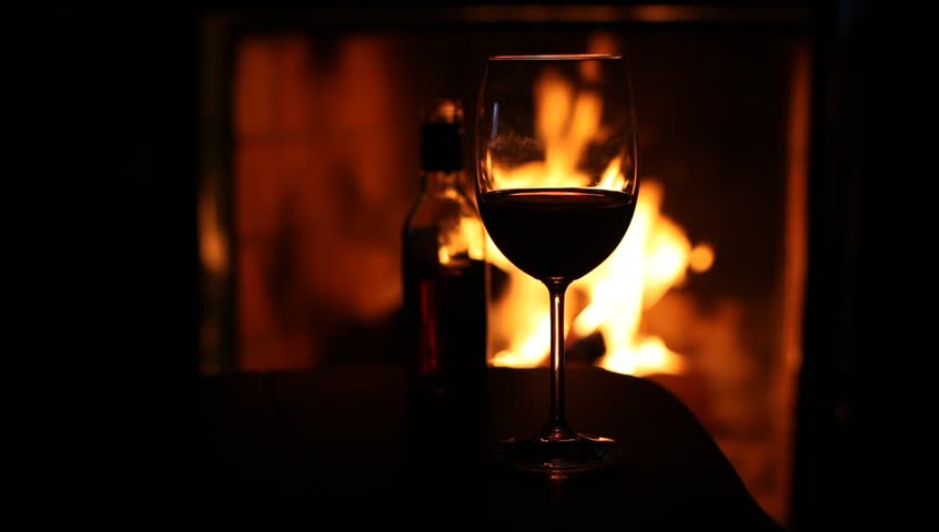 A Glass Of Red Wine And A Wine Bottle With A Woman Stoking A Fire In ...