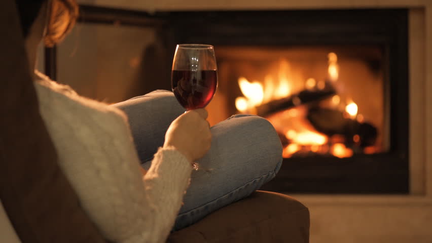 Young Woman Sitting At Home By The Fireplace And Drinking A Red Wine