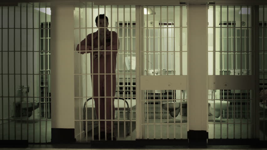 Inmate Gets Up From Bed To Stand At The Bars Of His Prison Cell ...